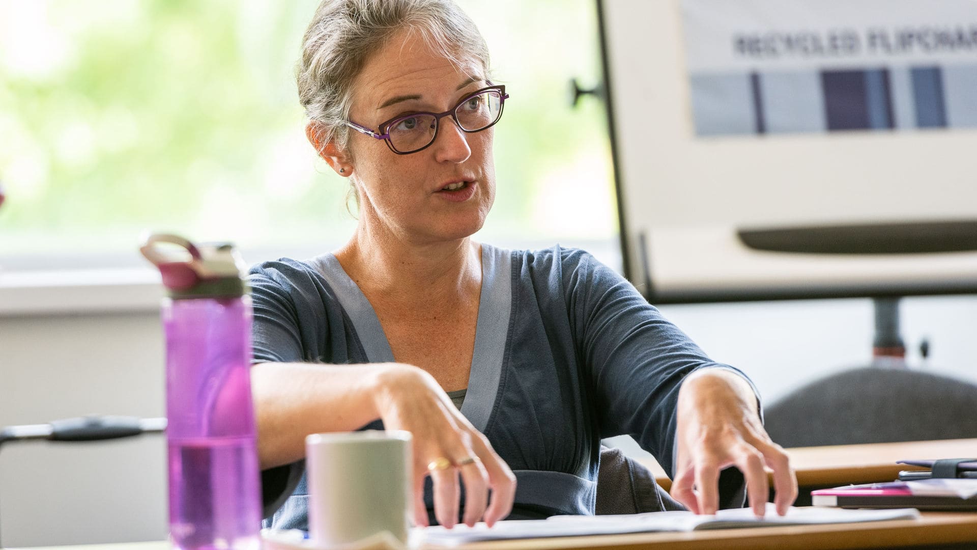 Seated woman with glasses gesturing with her hands.