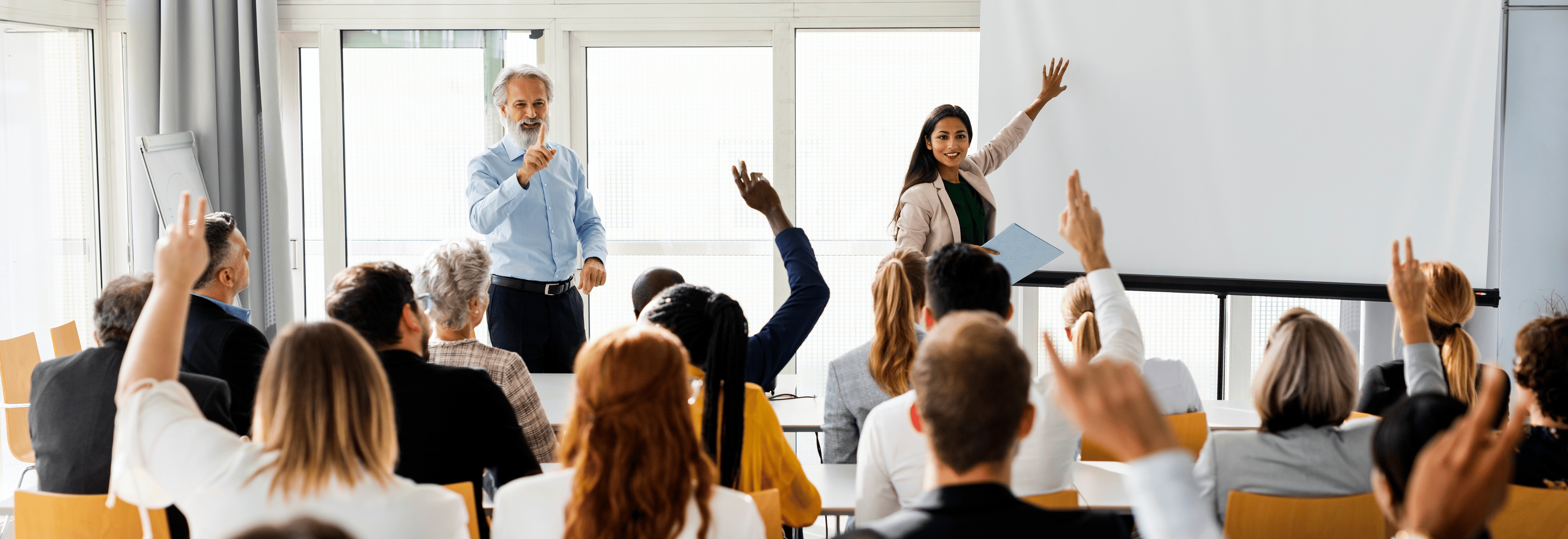 Students raise their hands whilst a lecturer stands at the white board.